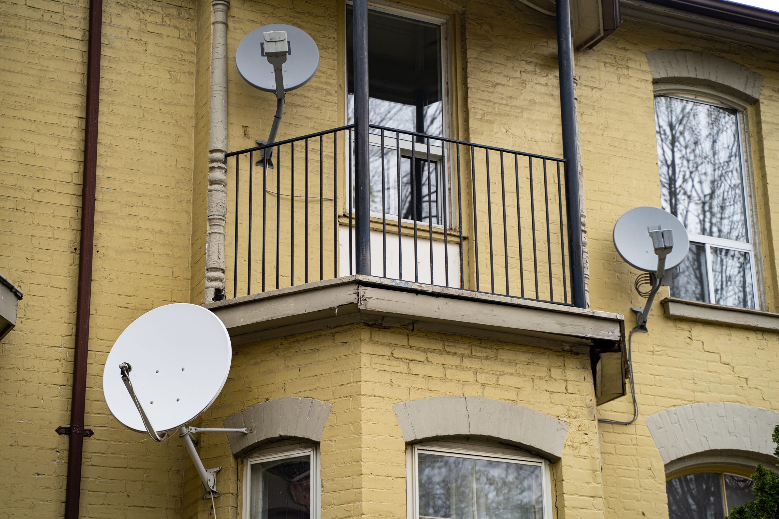 View,Of,Yellow,Brick,Building,Facade,With,Balcony,And,Satellite sattelite dishes