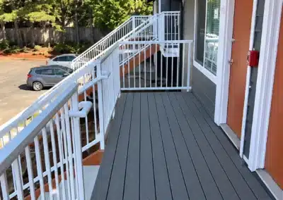 Second-floor walkway with new decking and white railings beside apartment entry doors